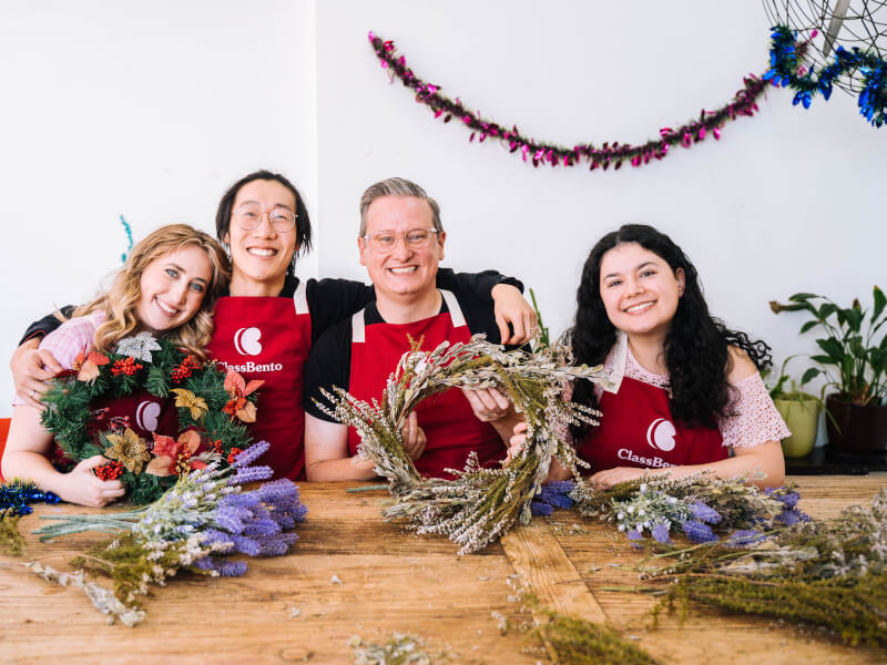 A group of people smile as they hold up the work made in a wreath class.